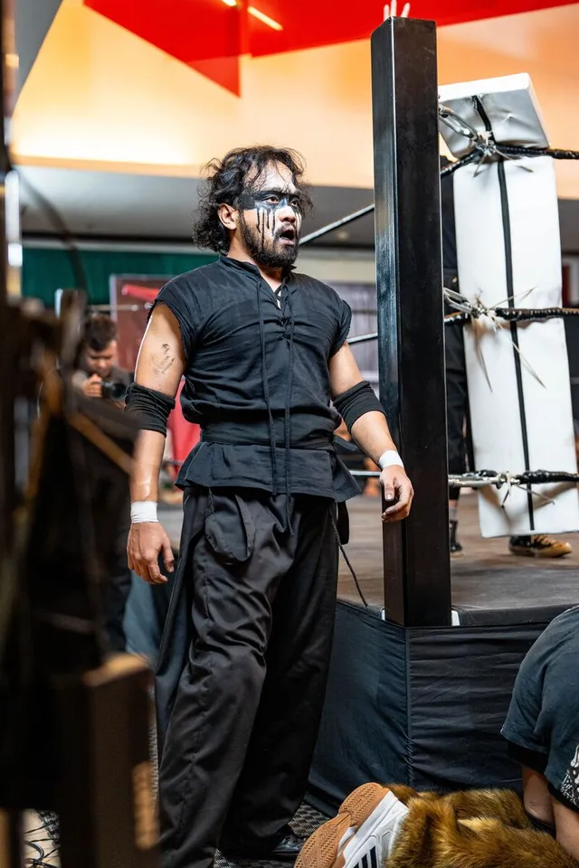 A wrestler in corpse paint stares down the ring from the floor