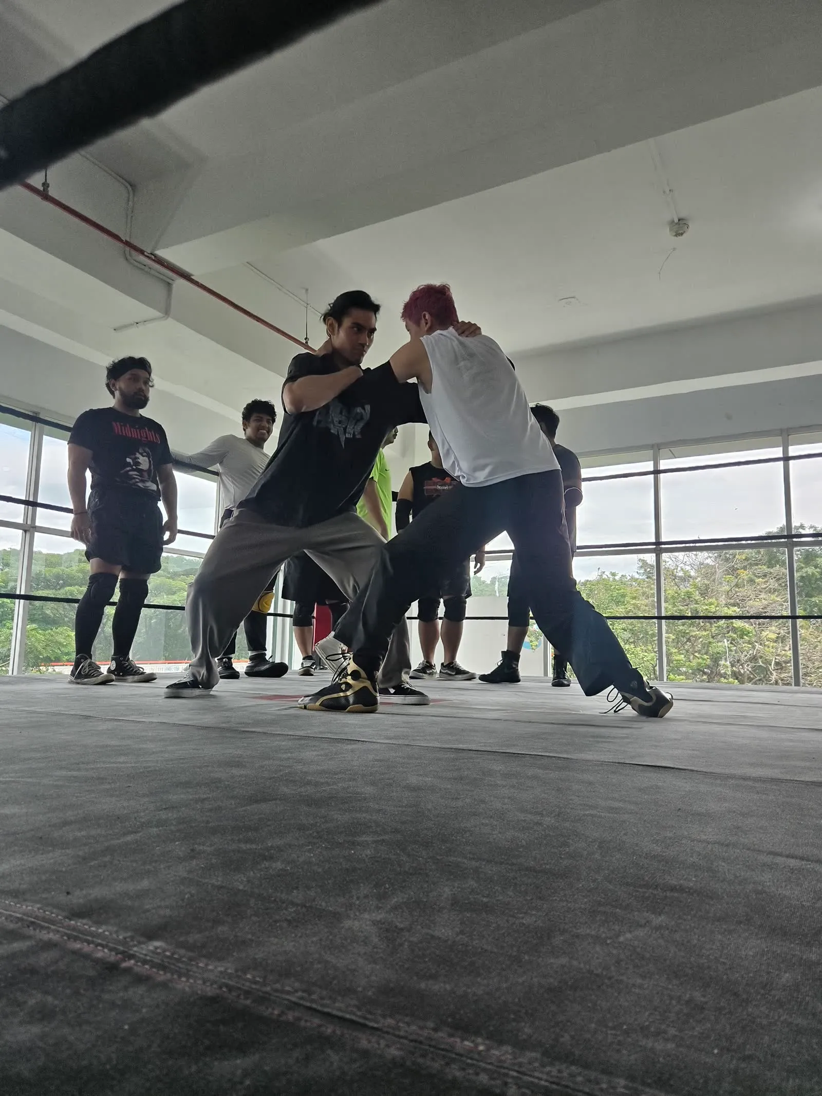 Two IDPW trainees locked up in a standing grapple while classmates watch inside the training ring